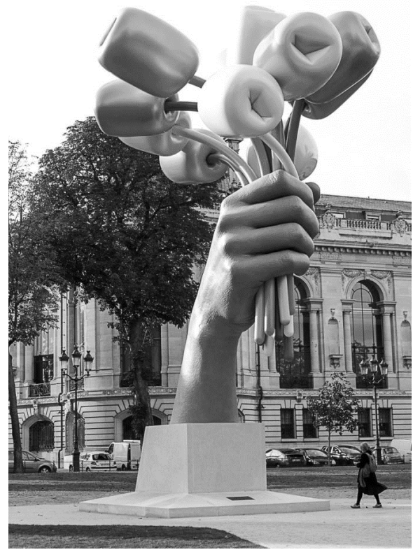 Skulptur einer Hand, die mehrere Blumen hält, vor einem historischen Gebäude.